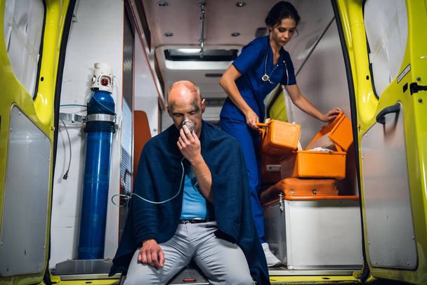Mann atmet durch Sauerstoffmaske, Krankenschwester öffnet Arzttasche im Rettungswagen - Foto, Bild