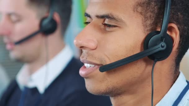 Primer plano del hombre de raza mixta con auriculares hablando con alguien en la oficina
 - Imágenes, Vídeo