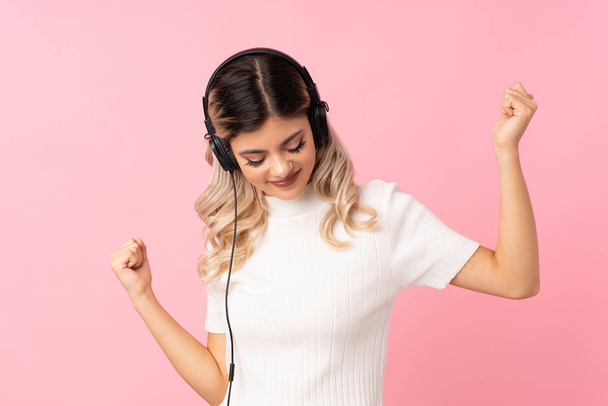 Teenager dívka přes izolované růžové pozadí pomocí mobilu se sluchátky a tancem - Fotografie, Obrázek
