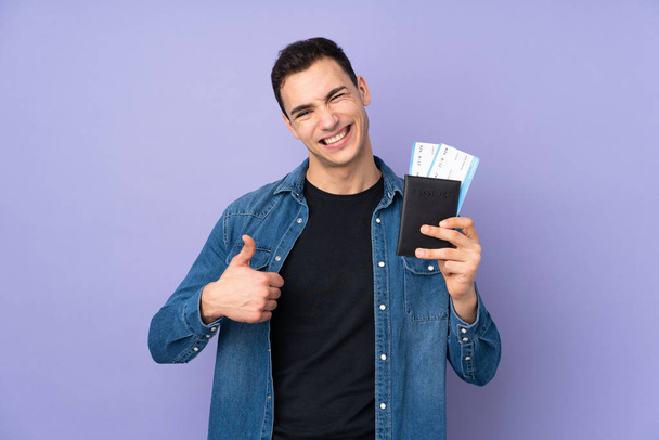 Young caucasian handsome man isolated on purple background in vacation holding a passport and plane with thumb up - Foto, imagen