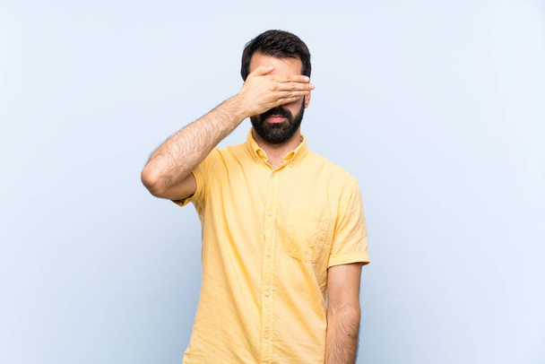 Young man with beard over isolated blue background covering eyes by hands. Do not want to see something - Photo, Image