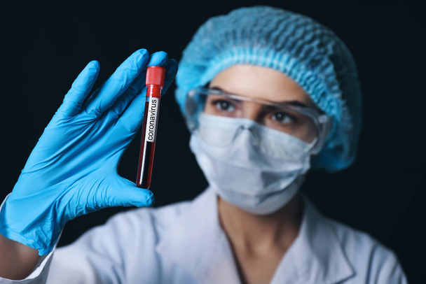 Female doctor holding blood sample in test tube with text CORONAVIRUS on dark background - Zdjęcie, obraz