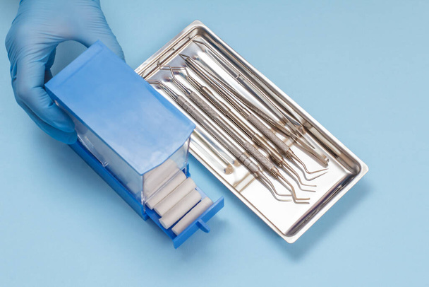 Рука дантиста с коробкой и набором металлических стоматологических инструментов для ухода за зубами
 - Фото, изображение