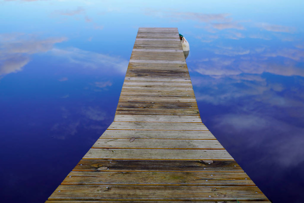wooden pontoon on blue lake seems to float in the sky with image mirror reflection - Photo, Image