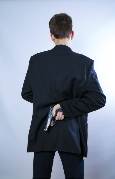 A man holding a gun on his back. The gunman held his gun behind him.Crime Concept.Criminality Concept. Back view - Zdjęcie, obraz