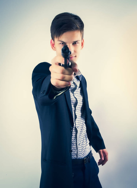 Portrait of young man wearing a business attire holding a gun in front of him. Isolated on bright. Selective focus. - Photo, Image