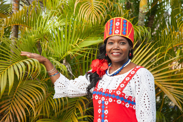 Portrait of a happy African-American woman in a bright colorful national Russian dress posing in the garden against a background of beautiful green palm trees. Traditions, fashion, world tourism. - Photo, Image