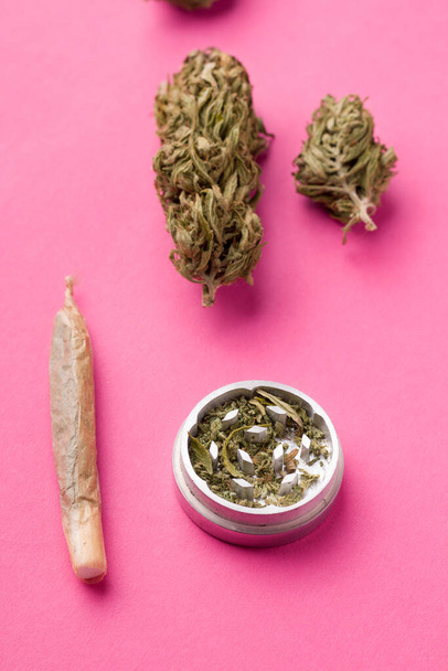 een jamb met marihuana en hele hennep naast een molen op een roze achtergrond - Foto, afbeelding