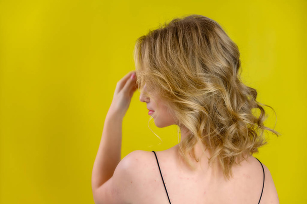 Glamorous beauty rear view portrait of a pretty model with blond hair with great makeup and a beautiful hairstyle on a yellow background in the studio. The concept of cosmetics, fashion and style. - Fotografie, Obrázek