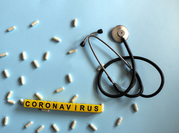pills, stethoscope, thermometer, inhalation mask on a blue background with children`s yellow letters. Coronavirus 2019-nCoV disease and treatment concept. - 写真・画像