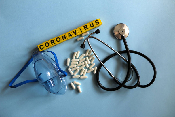 Pillen, Stethoskop, Thermometer, Inhalationsmaske auf blauem Grund mit gelben Kinderbuchstaben. Coronavirus 2019-ncov-Krankheit und Behandlungskonzept. - Foto, Bild