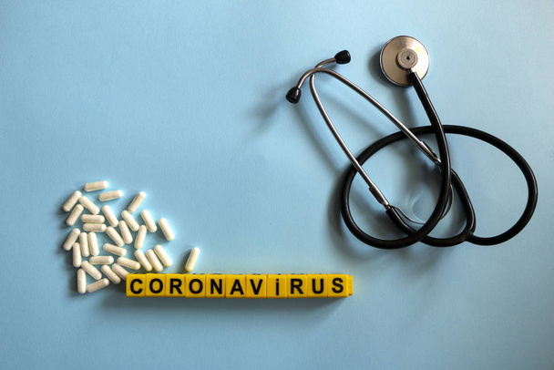 pills, stethoscope, thermometer, inhalation mask on a blue background with children`s yellow letters. Coronavirus 2019-nCoV disease and treatment concept. - Photo, image