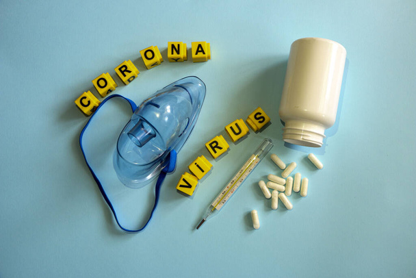 pills, stethoscope, thermometer, inhalation mask on a blue background with children`s yellow letters. Coronavirus 2019-nCoV disease and treatment concept. - Фото, зображення