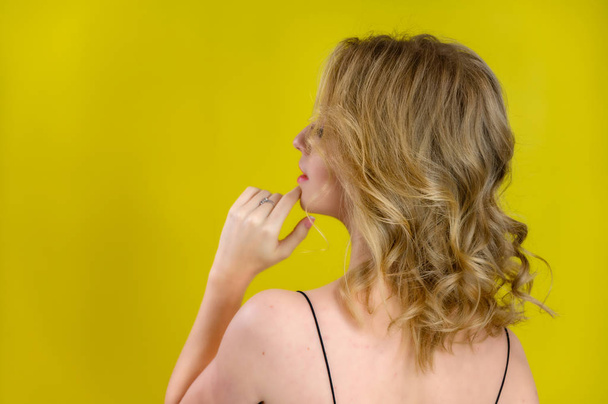 Glamorous beauty rear view portrait of a pretty model with blond hair with great makeup and a beautiful hairstyle on a yellow background in the studio. The concept of cosmetics, fashion and style. - Φωτογραφία, εικόνα