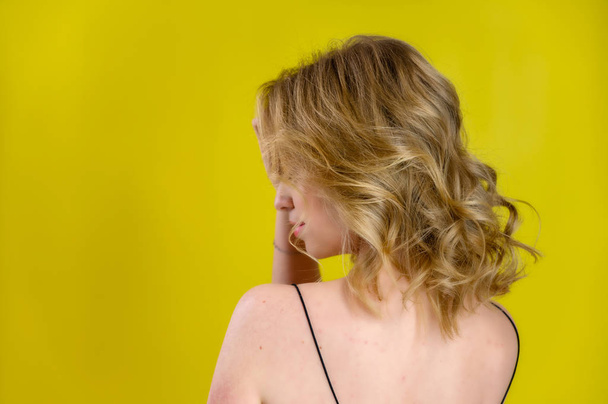 Glamorous beauty rear view portrait of a pretty model with blond hair with great makeup and a beautiful hairstyle on a yellow background in the studio. The concept of cosmetics, fashion and style. - Fotoğraf, Görsel