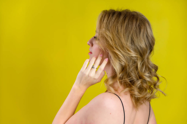 Glamorous beauty rear view portrait of a pretty model with blond hair with great makeup and a beautiful hairstyle on a yellow background in the studio. The concept of cosmetics, fashion and style. - Фото, изображение