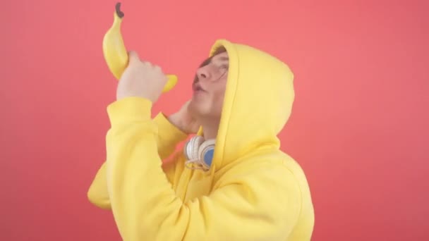 A young man in a sweatshirt sings in a banana on a red background - Materiaali, video