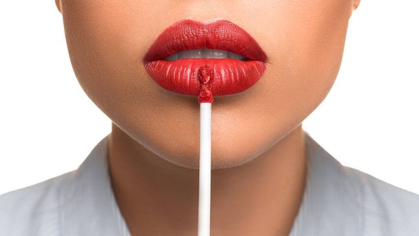 Νεαρή γυναίκα απλώνει ένα lip gloss στα χείλη της σε λευκό φόντο. - Φωτογραφία, εικόνα