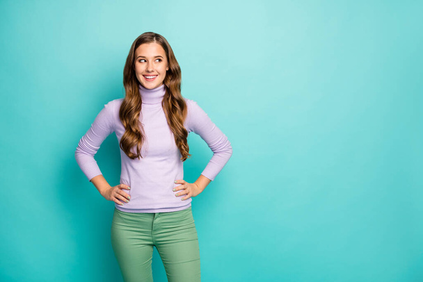 Photo of beautiful pretty lady long curly hairstyle good mood hands by sides look empty space wondered wear lilac purple sweater green trousers isolated pastel blue color background - Photo, Image