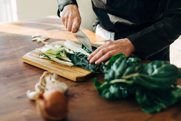 Female chef chopping raw vegetables on a wooden board - Fotó, kép