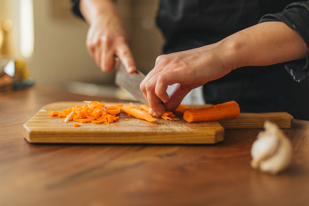 Female chef chopping carrot  on a wooden board - Foto, Imagen