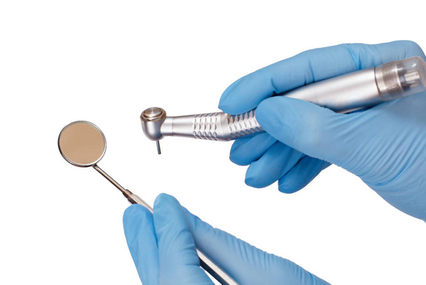 Dentist's hands in gloves with dental handpiece and mouth mirror. - Photo, Image