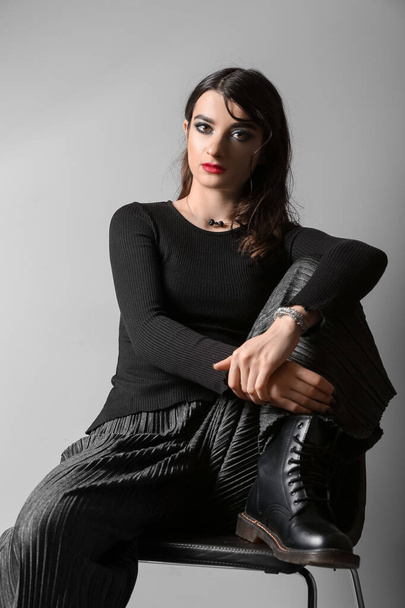 Beautiful fashionable woman sitting on chair against light background - Фото, зображення