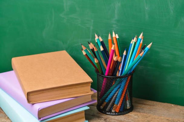 Ołówki i książki na stole w pobliżu tablicy szkolnej - Zdjęcie, obraz