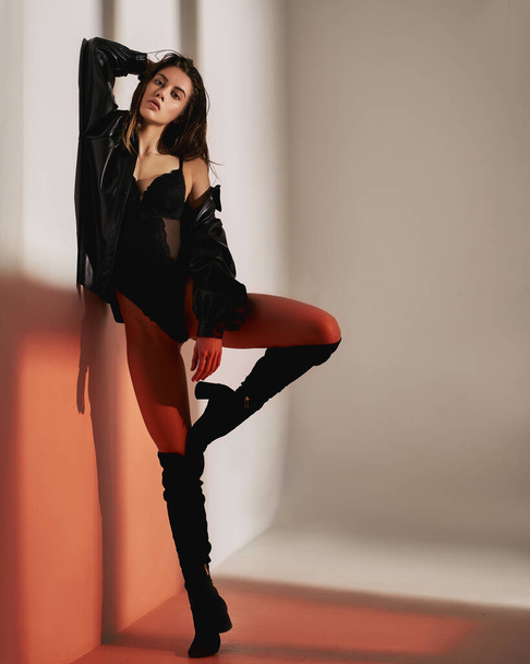Sexy donna stile moda in biancheria intima con giacca di pelle e stivali hessian in posa su sfondo bianco e rosso di ombra finestra in studio
 - Foto, immagini