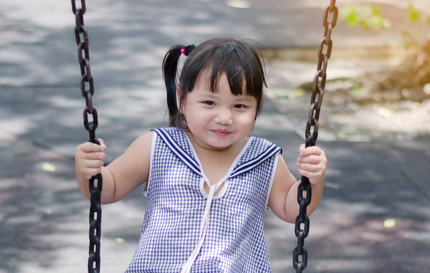 Una niña o un niño se sienten felices riendo y balanceándose en un columpio en el patio de recreo
. - Foto, Imagen