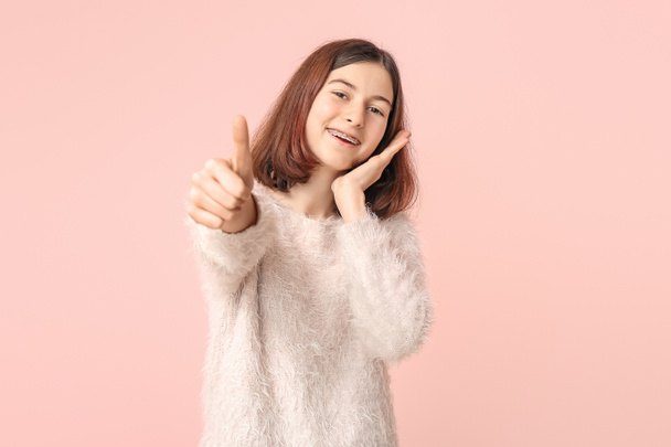 Teenage girl with dental braces showing thumb-up gesture on color background - Foto, afbeelding