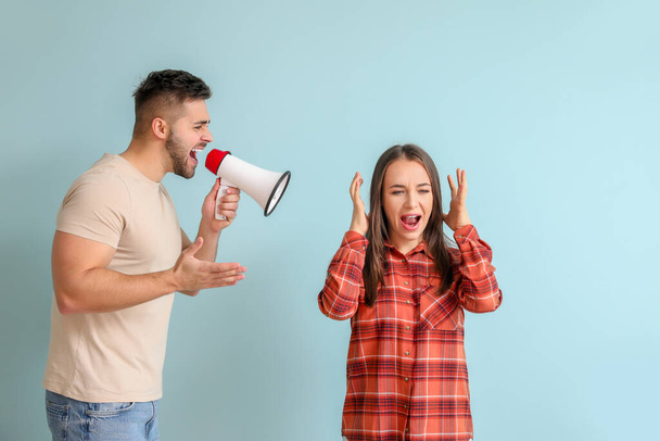 Angry man with megaphone shouting at his wife on color background - Foto, Imagen