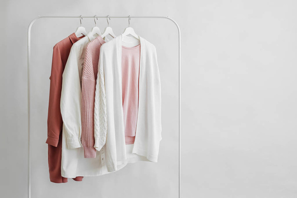 Feminine clothes in pastel pink  color on hanger on white background.  Elegant dress,  jumper, shirt and other fashion outfit. Spring cleaning home wardrobe. Minimal concept. - Photo, image