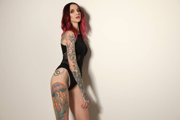 Beautiful woman with tattoos on body against light background. Space for text - Foto, Imagem