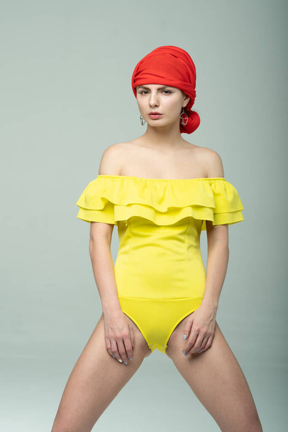 young beautiful girl pose in a yellow bodysuit in the studio - Фото, изображение