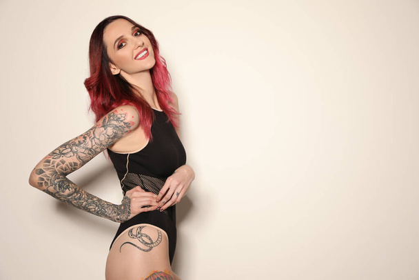 Beautiful woman with tattoos on body against light background. Space for text - 写真・画像