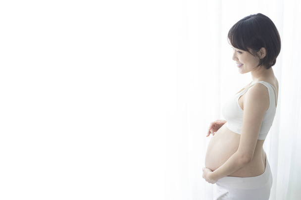 Young pregnant Asian woman standing half a turn and holding on to her belly. - Foto, immagini