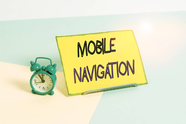 Text sign showing Mobile Navigation. Business photo showcasing graphical user interface used to aid the vehicle driver Mini size alarm clock beside a Paper sheet placed tilted on pastel backdrop - Photo, Image