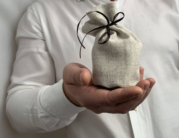 Una bolsa con un signo de dólar en la mano de un hombre de negocios. Un hombre tiene una arpillera en sus manos. Un hombre de negocios muestra un signo de riqueza. Concepto: inversión, éxito material
 - Foto, imagen