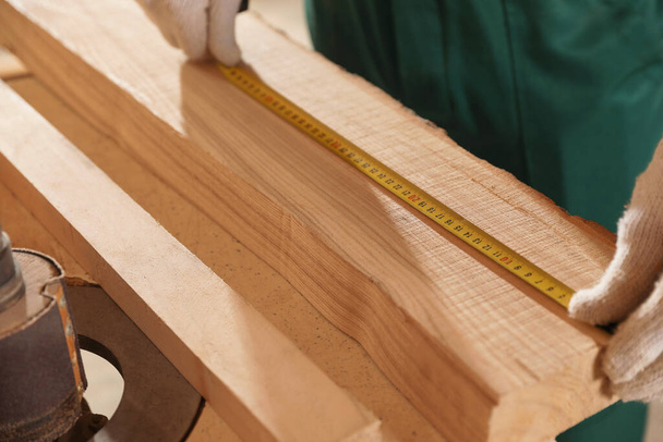 Professional carpenter measuring wooden board at workbench, closeup - Photo, image