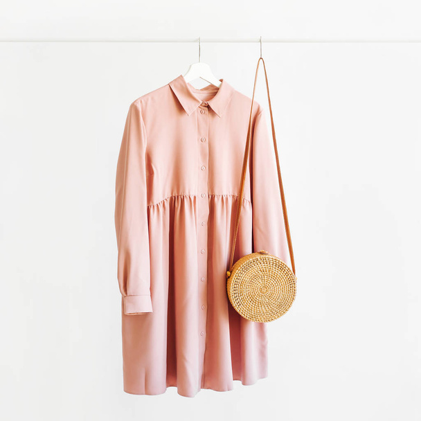 Pale pink dress with bamboo bag on hanger on white background. Elegant   fashion outfit. Spring wardrobe. Minimal concept. - Foto, Imagem