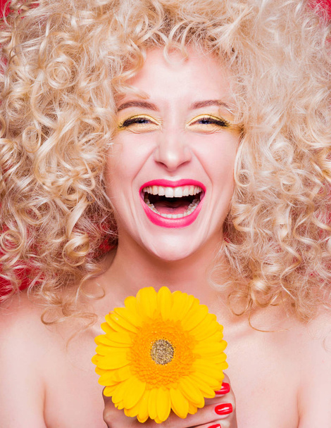 Krásná módní blondýnka v retro stylu s objemným kudrnatým účesem, holými rameny a slunečnicí v rukou na červeném pozadí. Šťastná dívka smích - Fotografie, Obrázek