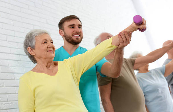 Care worker helping elderly woman to do exercise with dumbbell i - Photo, image