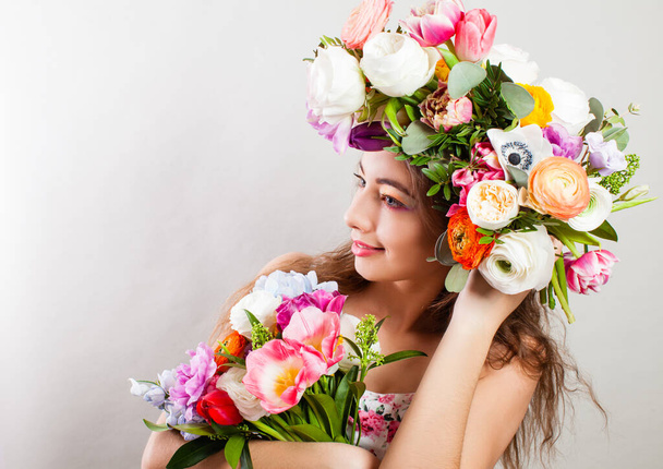 Beautiful young smiling model with bright flowers on her head - Фото, изображение