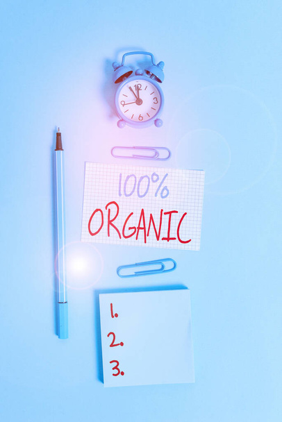Conceptual hand writing showing 100 Percent Organic. Concept meaning ingredients are certified no artificial food additives Alarm clock squared paper notepad marker clips colored background - Photo, Image