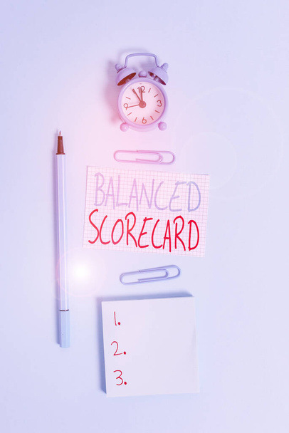 Conceptual hand writing showing Balanced Scorecard. Concept meaning a perforanalysisce metric used in strategic analysisment Alarm clock squared paper notepad marker clips colored background - Photo, Image