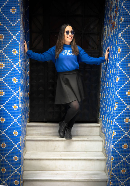 Girl in blue is posing on the stairs with hands touching the blue wall. Balat,Istanbul. Black background. Blank space above. Forget the rules. - Photo, Image