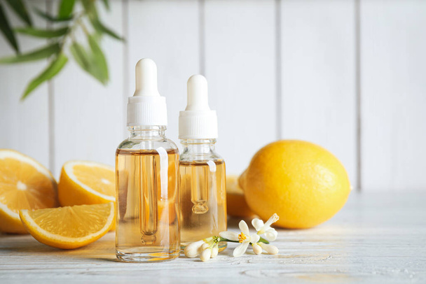 Bottles of citrus essential oil, flower and lemons on white wooden table. Space for text - Foto, imagen
