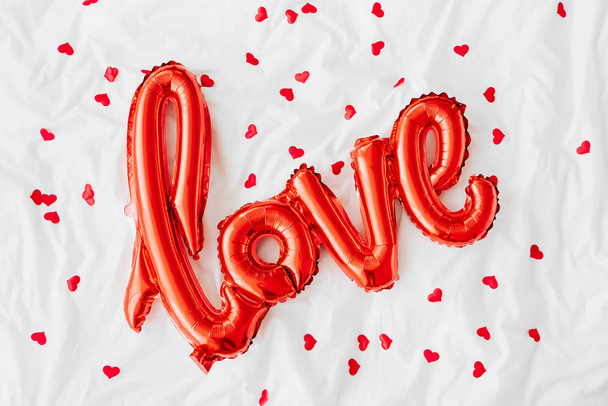 Red Air Balloons in the shape of the word "Love" with confetti on bed. Love concept. Holiday, celebration. Valentine's Day or wedding/bachelorette party decoration. Foil balloon - Zdjęcie, obraz