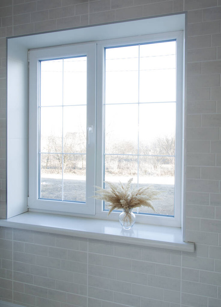 Fehér ablak az ablakpárkányon van egy váza száraz virágokkal. Belső tér - Fotó, kép